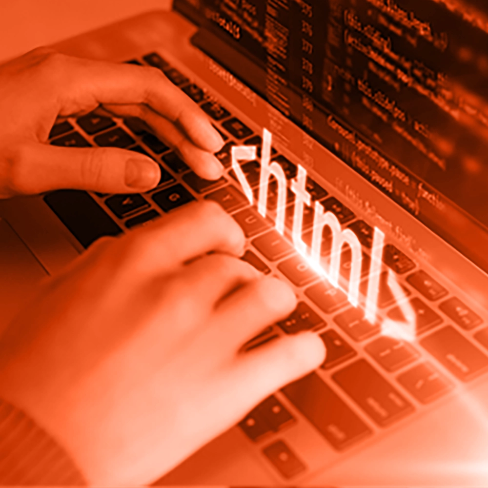 Employee’s hands on a laptop keyboard with “HTML” displayed, representing code review.